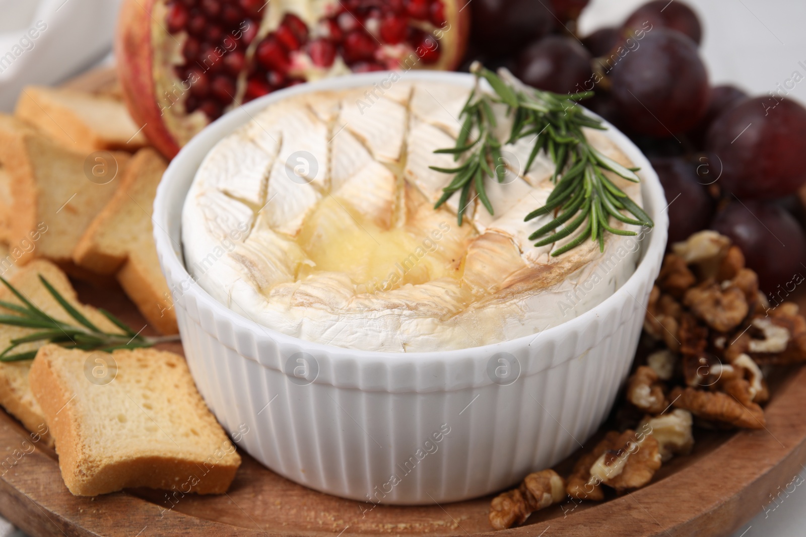 Photo of Board with tasty baked camembert, croutons, grapes, walnuts and pomegranate on table, closeup