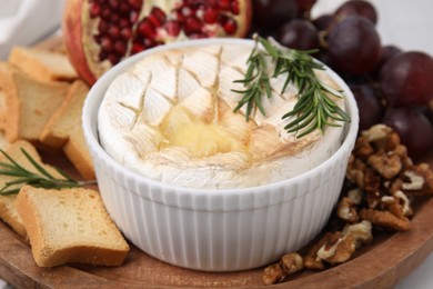 Photo of Board with tasty baked camembert, croutons, grapes, walnuts and pomegranate on table, closeup
