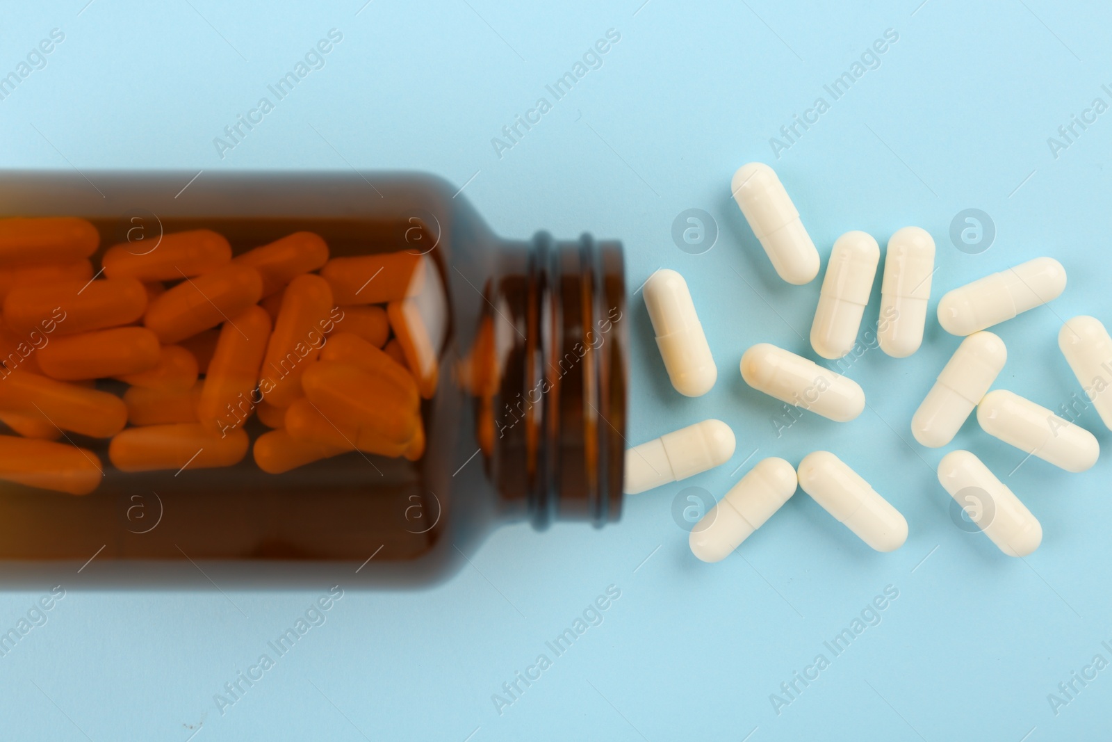 Photo of Bottle and vitamin capsules on light blue background, top view