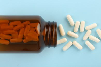 Bottle and vitamin capsules on light blue background, top view