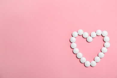 Heart made with white pills on color background