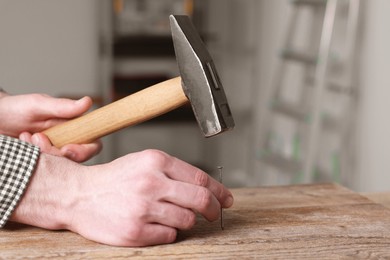 Photo of Professional repairman hammering nail into wooden board indoors, closeup