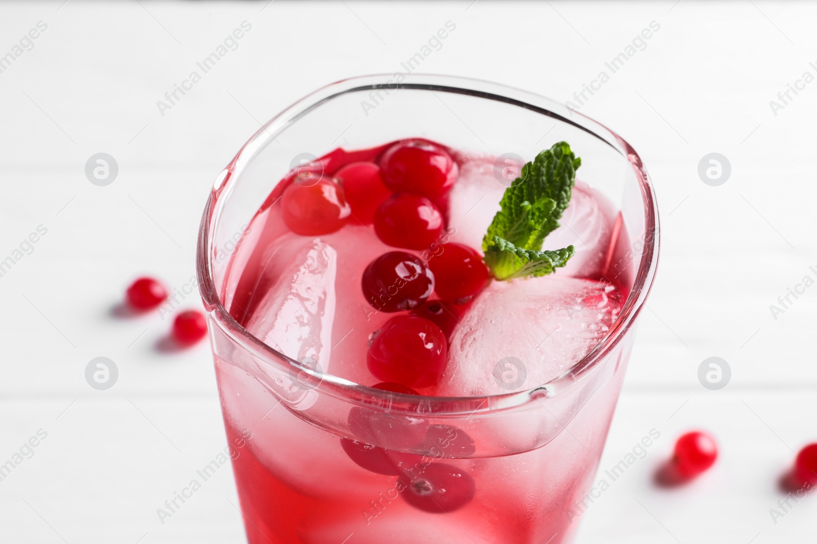 Photo of Tasty cranberry juice with ice cubes and mint in glass on white table, closeup