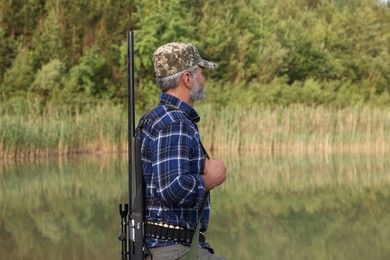 Man with hunting rifle near lake outdoors