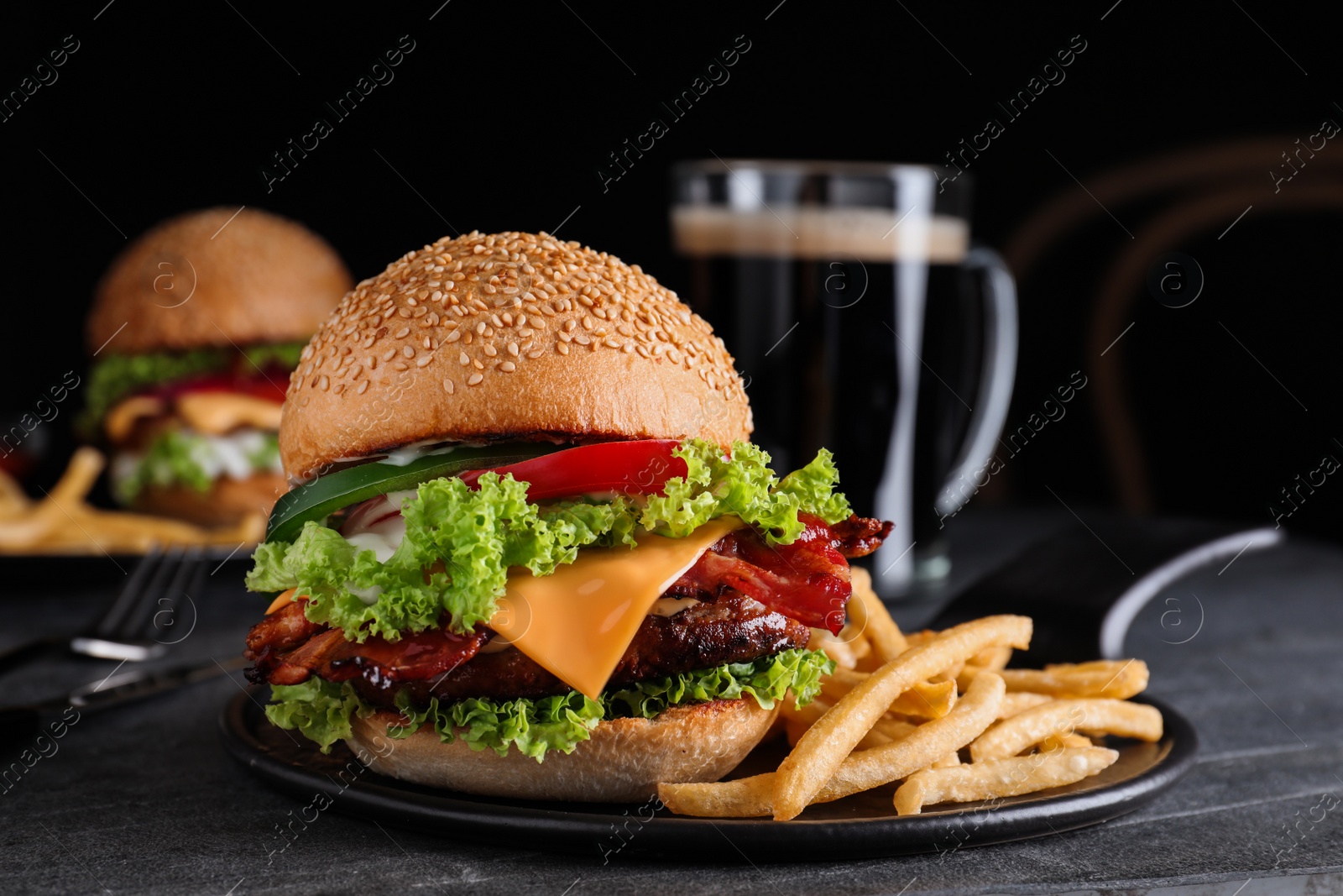 Photo of Fresh juicy bacon burger and fries on grey table