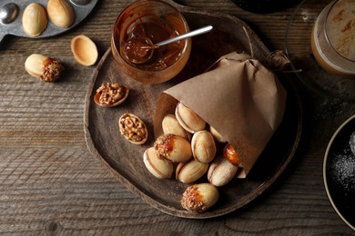 Freshly baked homemade walnut shaped cookies, boiled condensed milk and cup of coffee on wooden table, flat lay