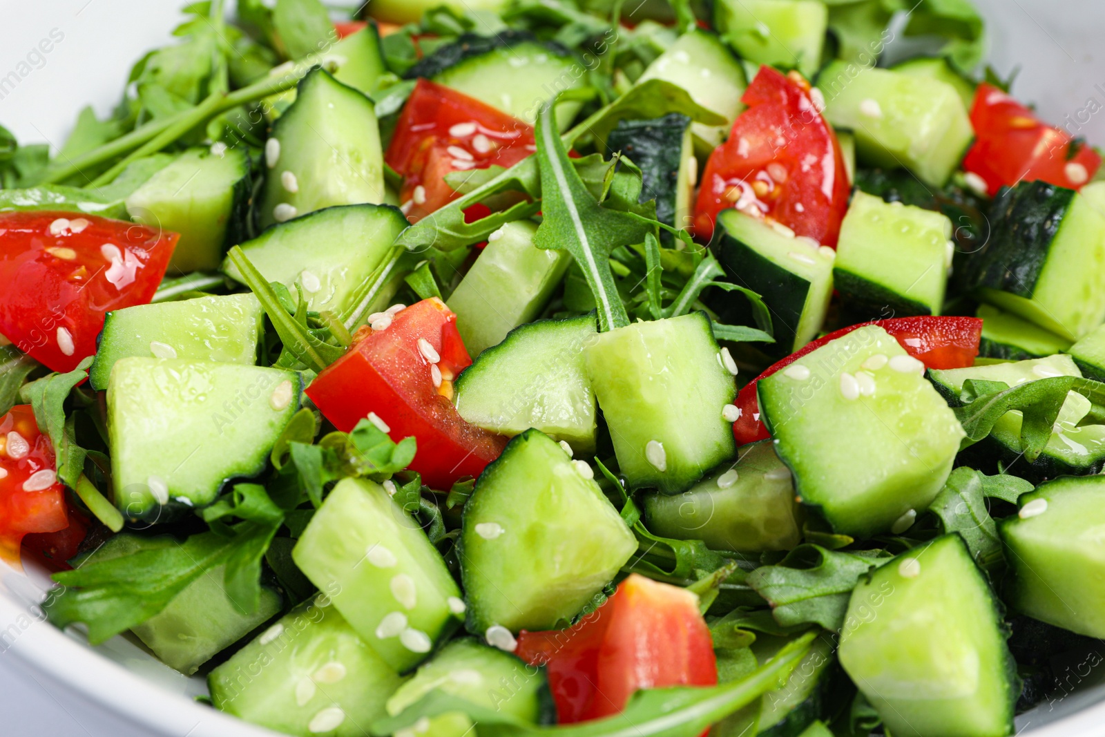 Photo of Delicious salad with cucumbers, tomatoes and sesame in bowl, closeup