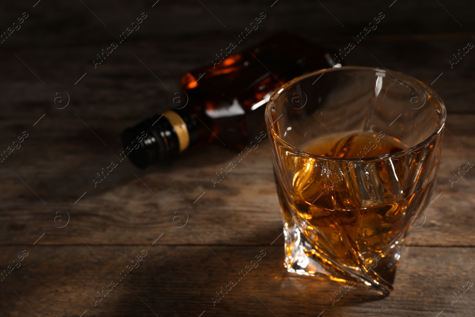 Photo of Golden whiskey in glass with ice cubes on table. Space for text