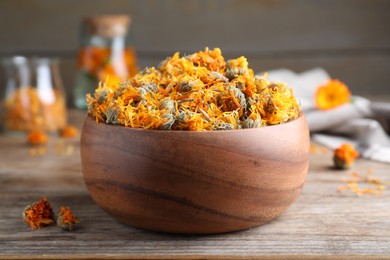 Photo of Bowl of dry calendula flowers on wooden table, closeup