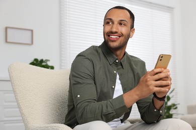 Happy man with smartphone sitting in armchair at home