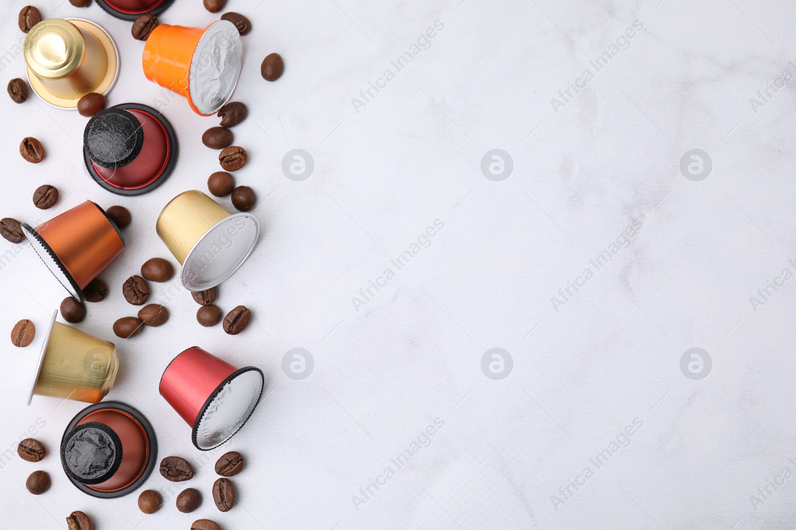 Photo of Many coffee capsules and beans on white marble table, flat lay. Space for text