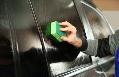 Worker washing tinted car window in shop, closeup