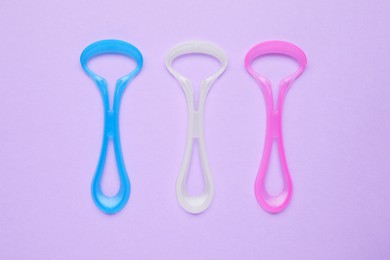 Photo of Colorful tongue cleaners on violet background, flat lay