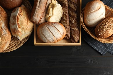 Wicker baskets with different types of fresh bread on black wooden table, flat lay. Space for text