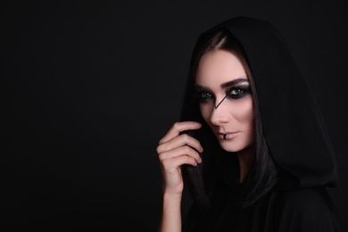 Photo of Mysterious witch in mantle with hood on black background. Space for text