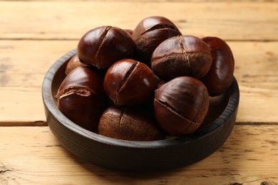 Photo of Fresh edible sweet chestnuts in bowl on wooden , closeup
