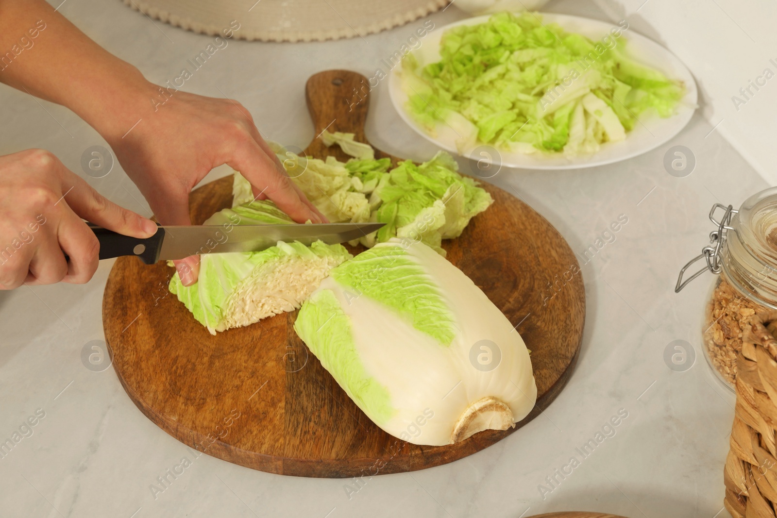 Photo of Woman cutting fresh chinese cabbage at kitchen table, closeup