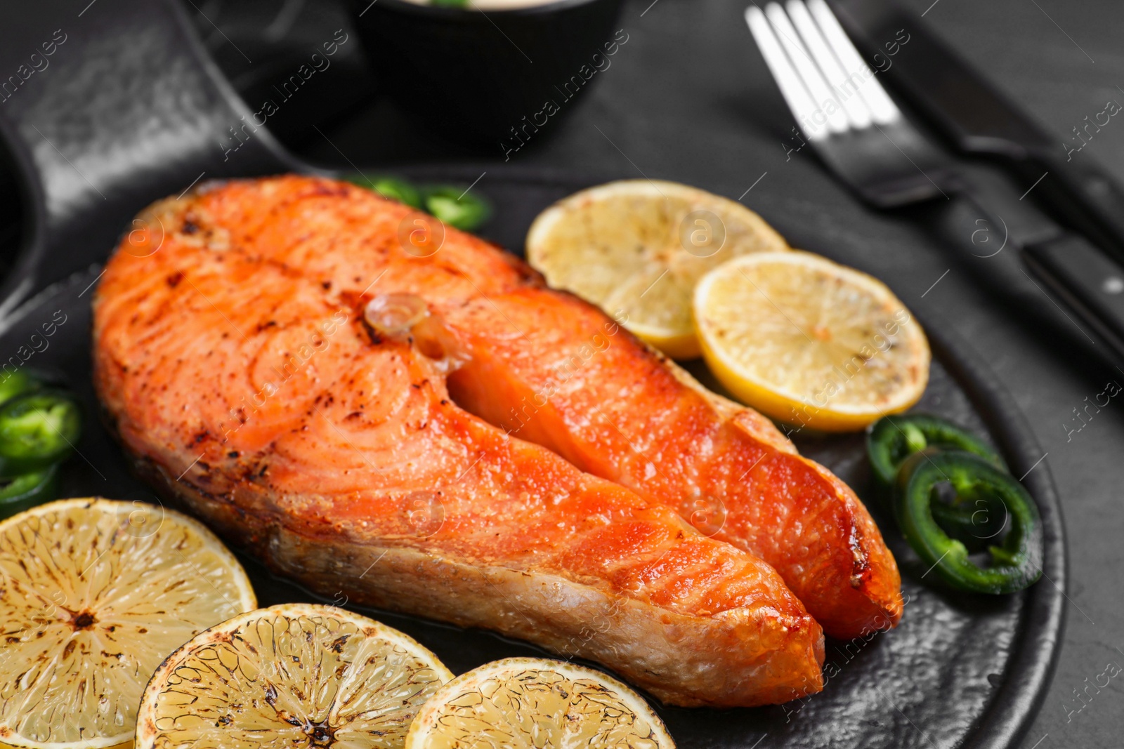 Photo of Delicious roasted fish served on black table, closeup