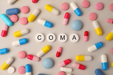 Pills with word Coma among others on beige background, flat lay