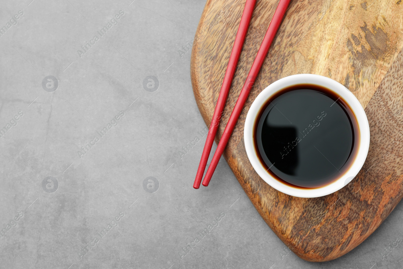 Photo of Bowl of soy sauce and chopsticks on grey table, top view. Space for text