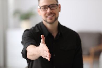Photo of Businessman reaching out for handshake indoors, focus on hand