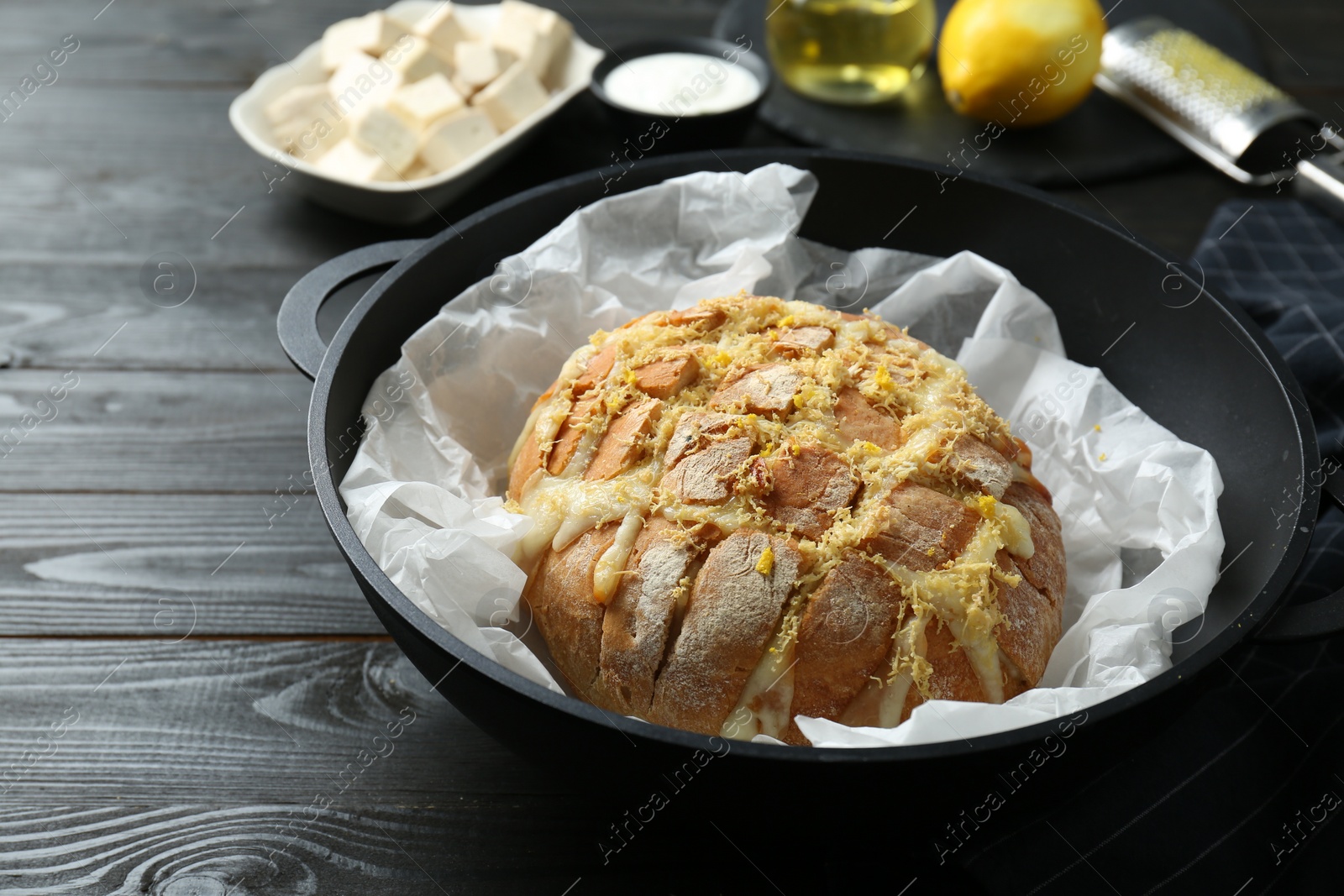 Photo of Freshly baked bread with tofu cheese and lemon zest on black wooden table, closeup