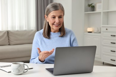 Photo of Happy woman having video chat via laptop at table indoors