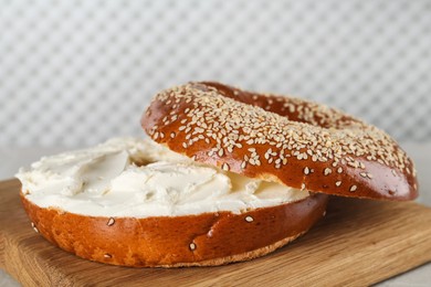 Photo of Delicious bagel with cream cheese on wooden board, closeup