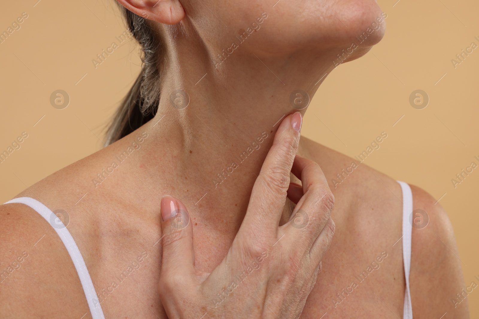 Photo of Mature woman touching her neck on beige background, closeup