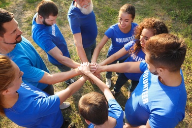 Photo of Group of volunteers joining hands together outdoors, above view