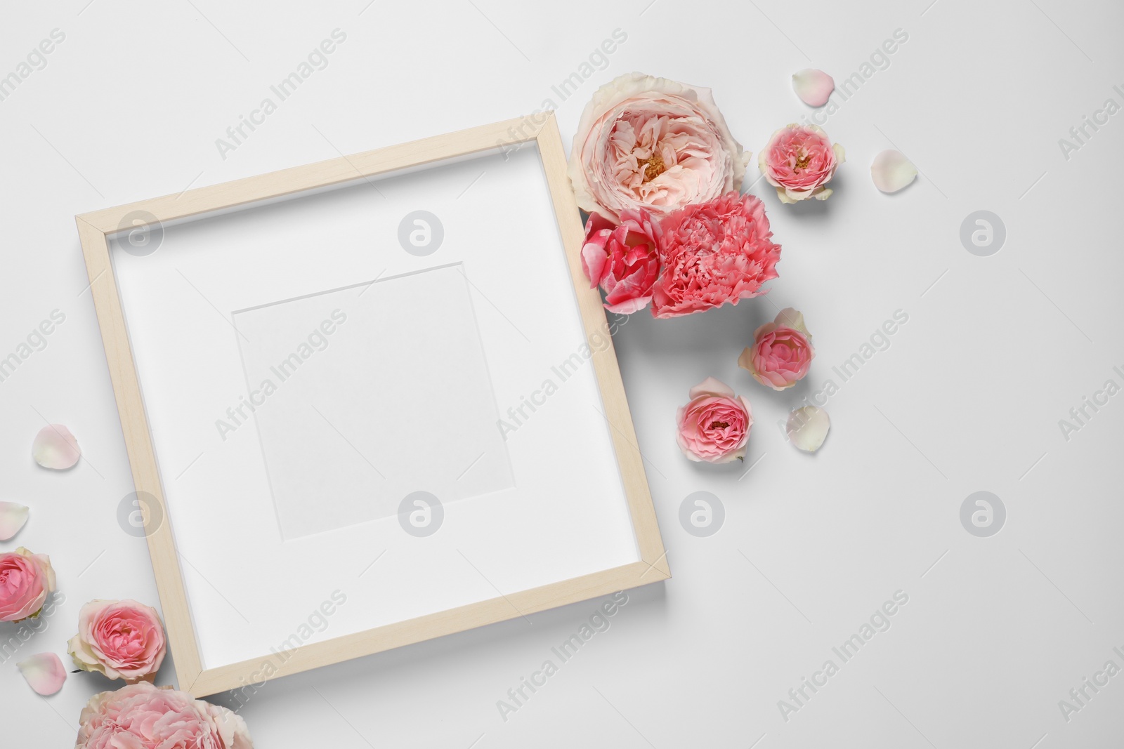 Photo of Empty photo frame and beautiful flowers on white background, flat lay. Space for design