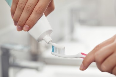 Photo of Woman applying toothpaste on brush in bathroom, closeup