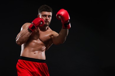 Photo of Man in boxing gloves fighting on black background. Space for text