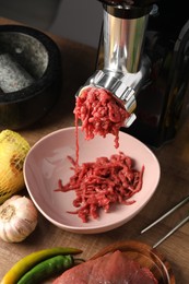 Mincing beef with electric meat grinder on wooden table