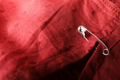 Photo of Metal safety pin on red fabric, closeup