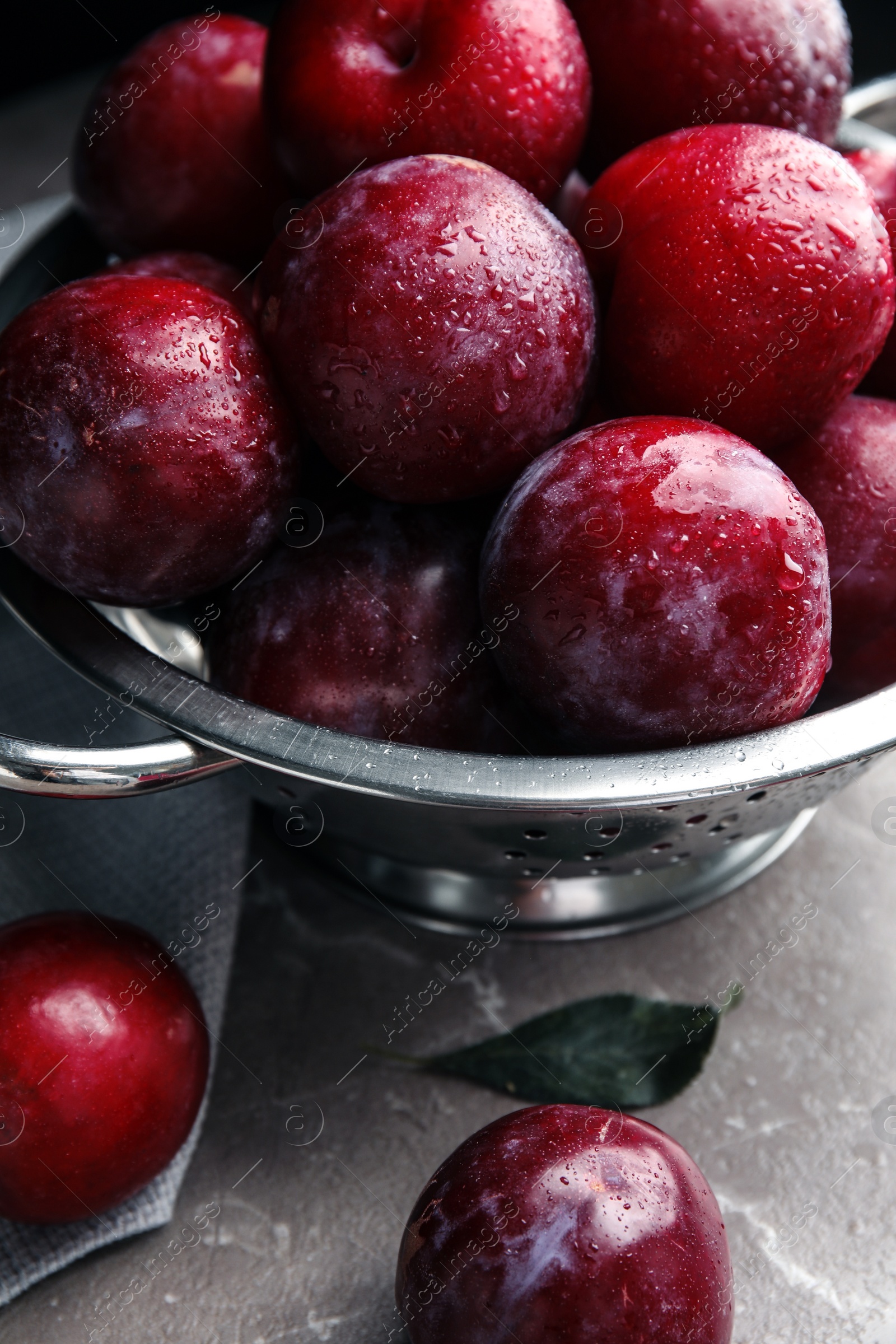 Photo of Delicious ripe plums in colander on grey marble table, closeup