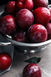 Delicious ripe plums in colander on grey marble table, closeup