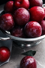 Photo of Delicious ripe plums in colander on grey marble table, closeup