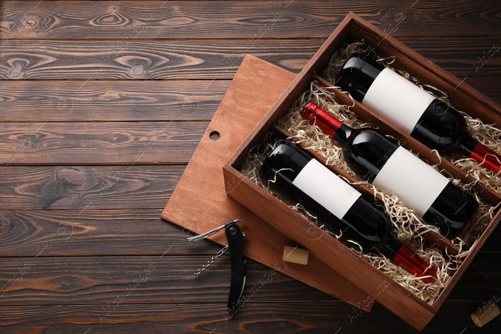 Photo of Box with wine bottles, corkscrew and corks on wooden table, flat lay. Space for text