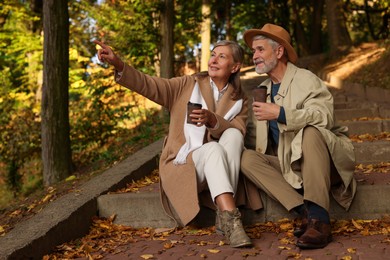 Photo of Affectionate senior couple with cups of coffee spending time together in autumn park
