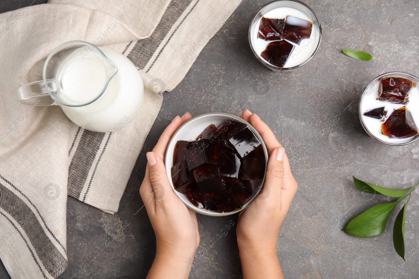 Photo of Woman holding glass of milk with delicious grass jelly at grey table, top view