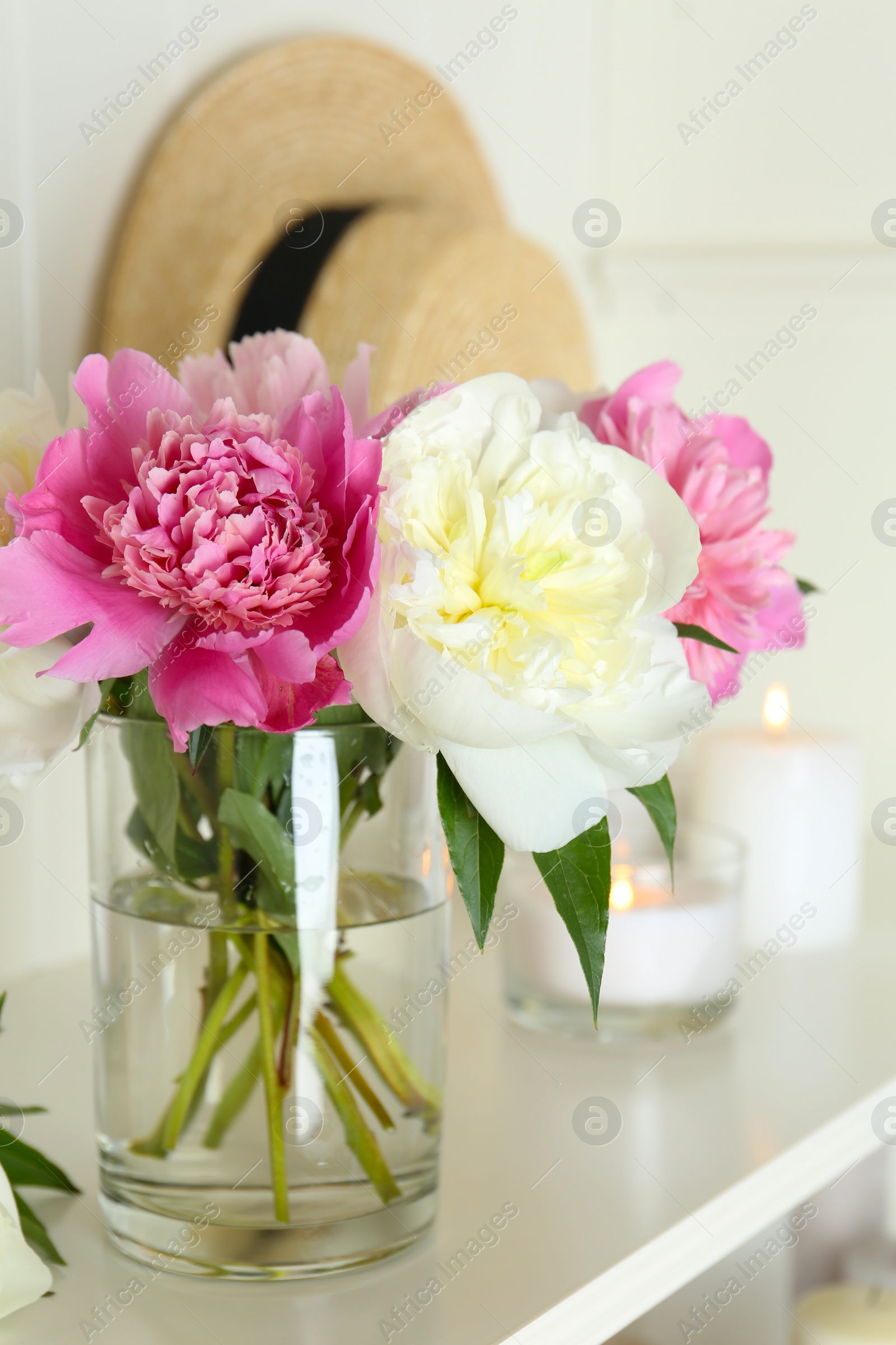 Photo of Bouquet of beautiful peonies in vase and candles on white table