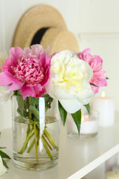 Bouquet of beautiful peonies in vase and candles on white table