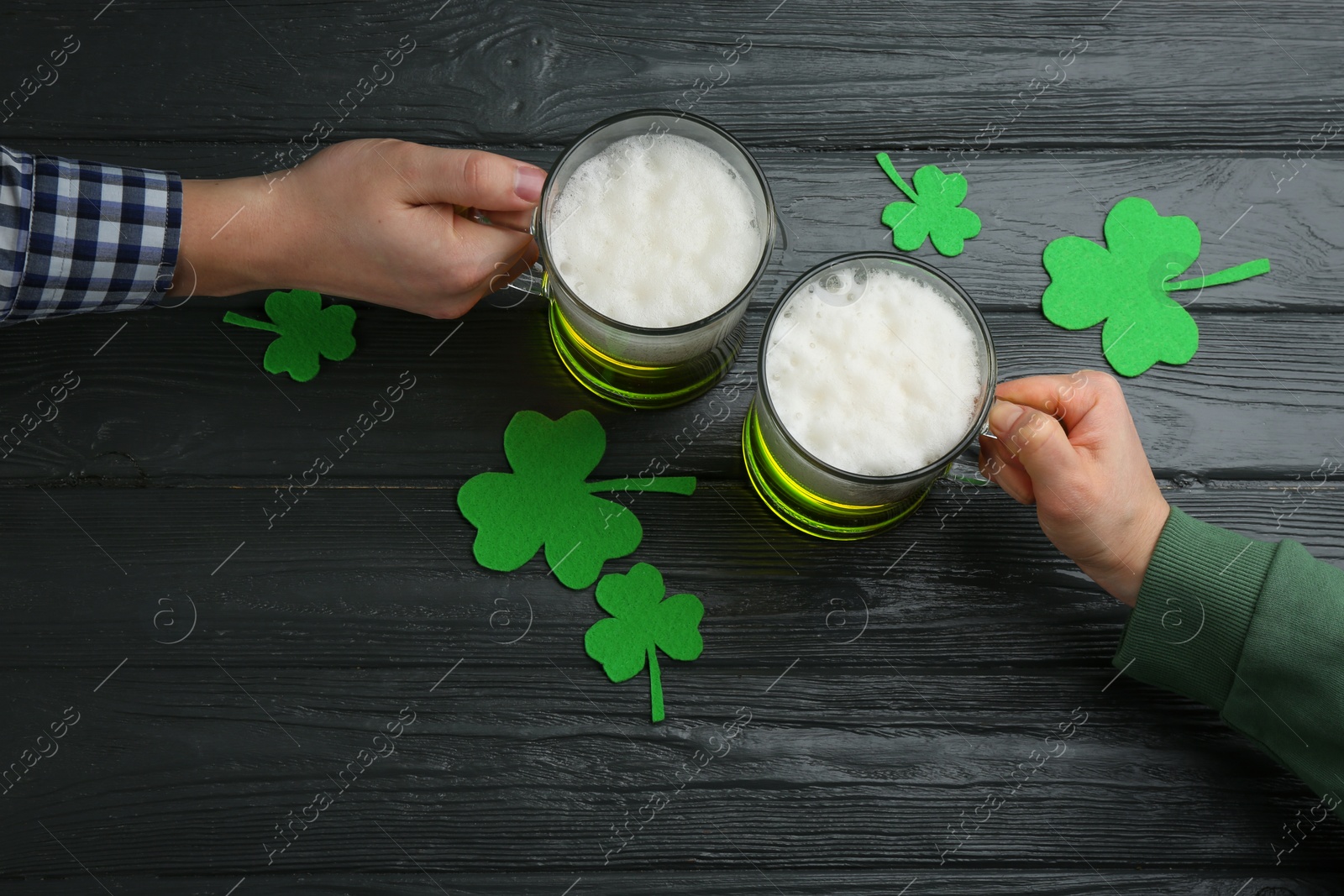 Photo of Man and woman toasting with green beer at black wooden table, top view. St. Patrick's Day celebration