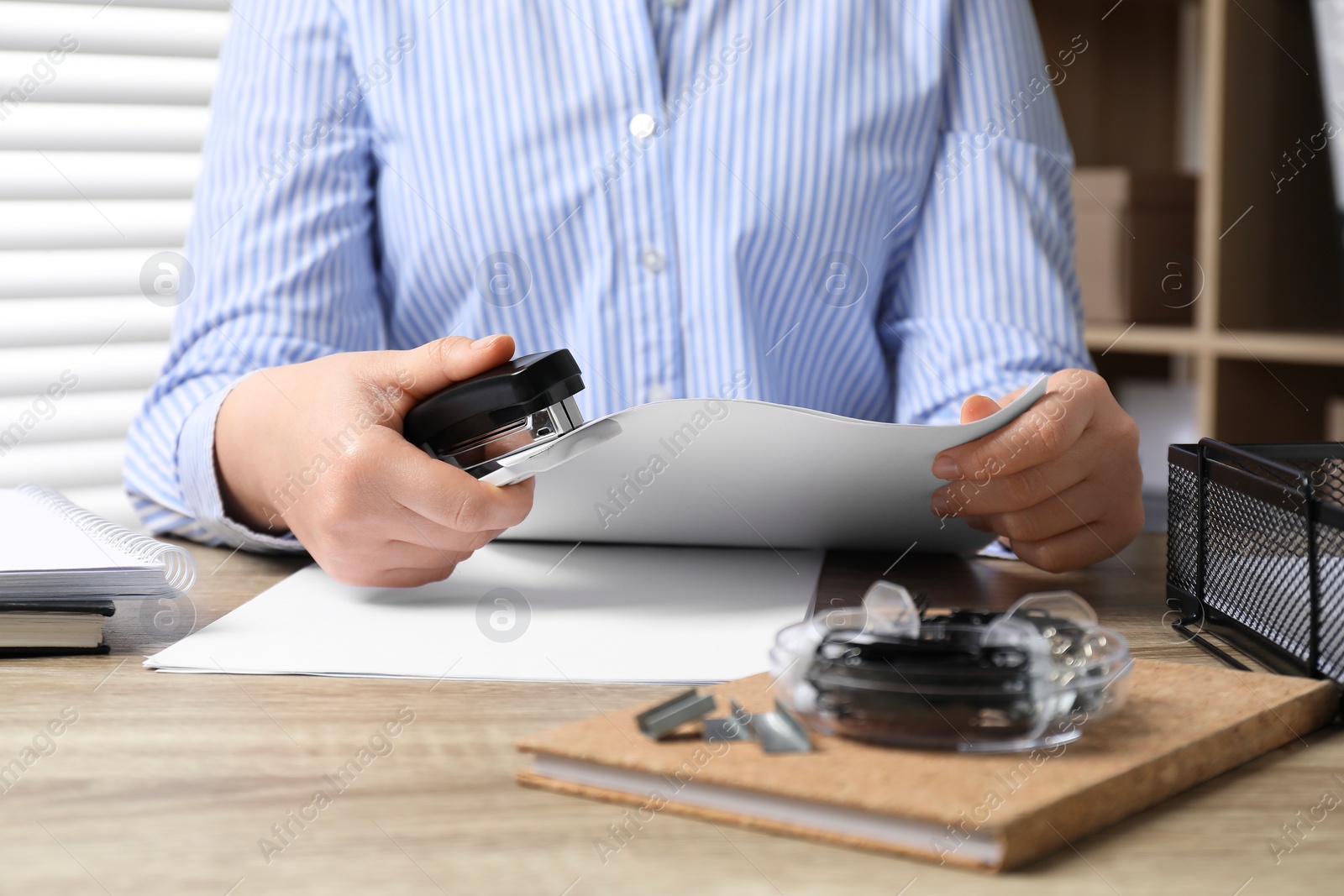 Photo of Woman with papers using stapler at wooden table indoors, closeup