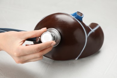 Photo of Doctor with stethoscope examining liver model at white table, closeup