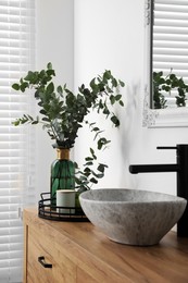 Photo of Beautiful eucalyptus branches near vessel sink on bathroom vanity. Interior design