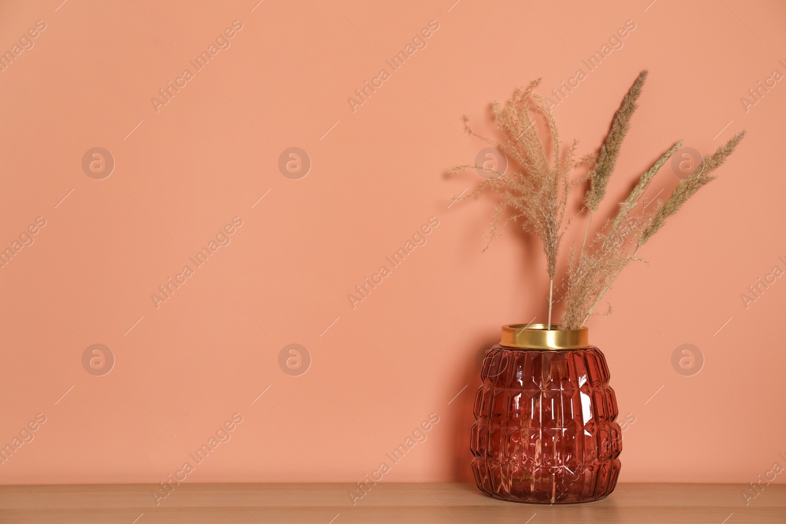 Photo of Stylish glass vase with dried flowers on table near brown wall. Space for text