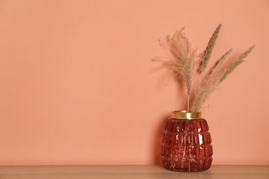 Photo of Stylish glass vase with dried flowers on table near brown wall. Space for text
