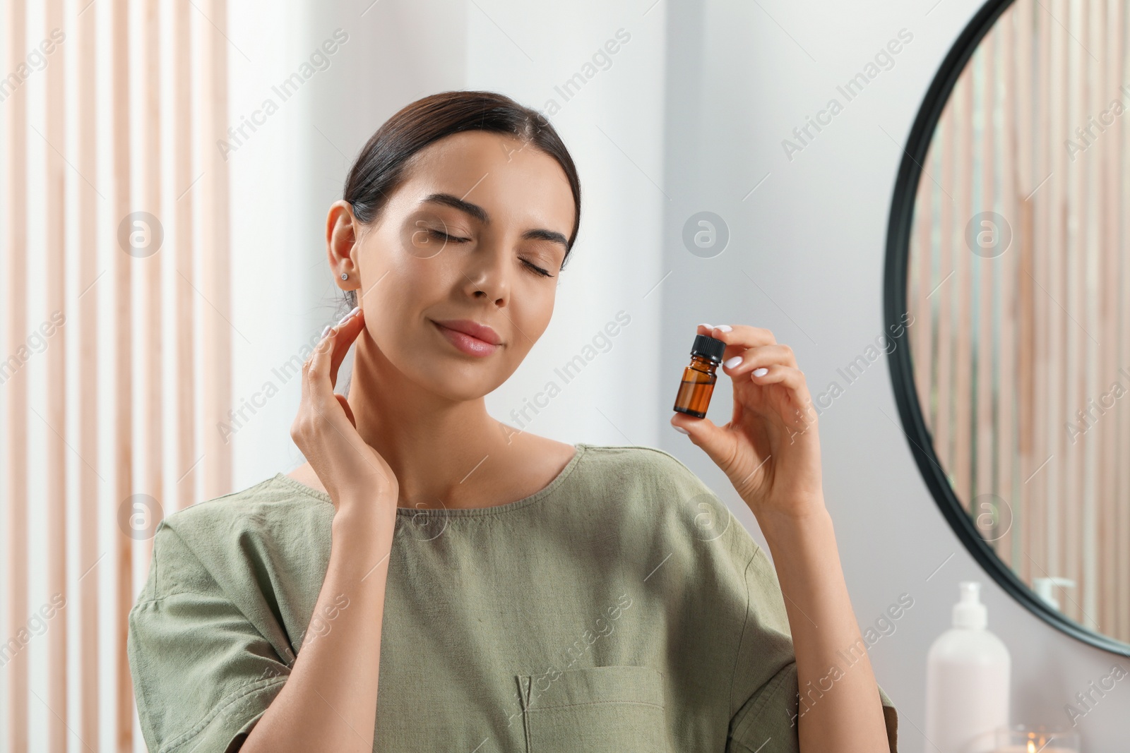 Photo of Young woman with bottle of essential oil indoors